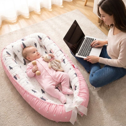 Maman travaillant sur son laptop avec son bébé allongé dans notre réducteur de lit bébé Cocon Sapin rose